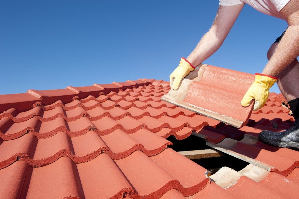 worker with yellow gloves replacing red tiles or shingles on house 