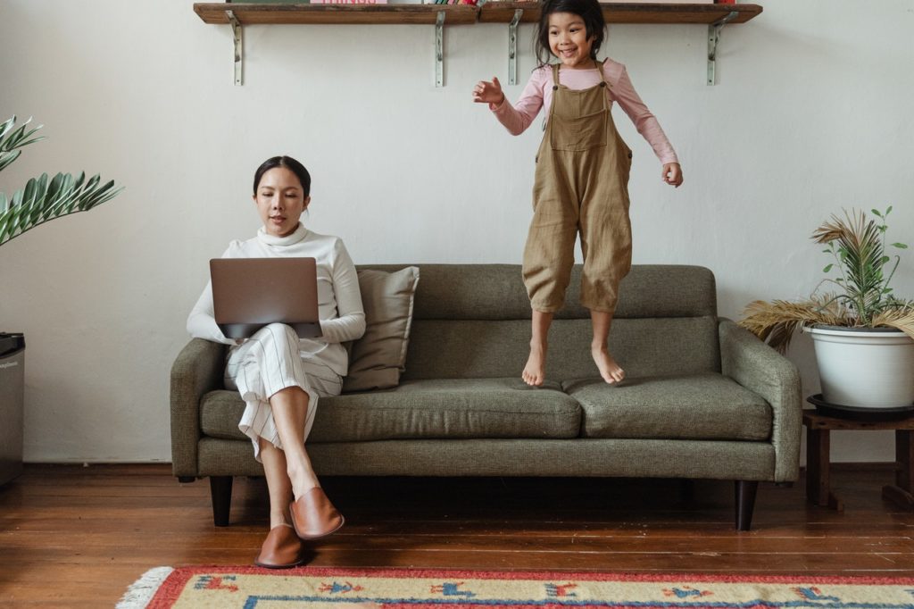 woman working from home on the couch with daughter jumping on couch